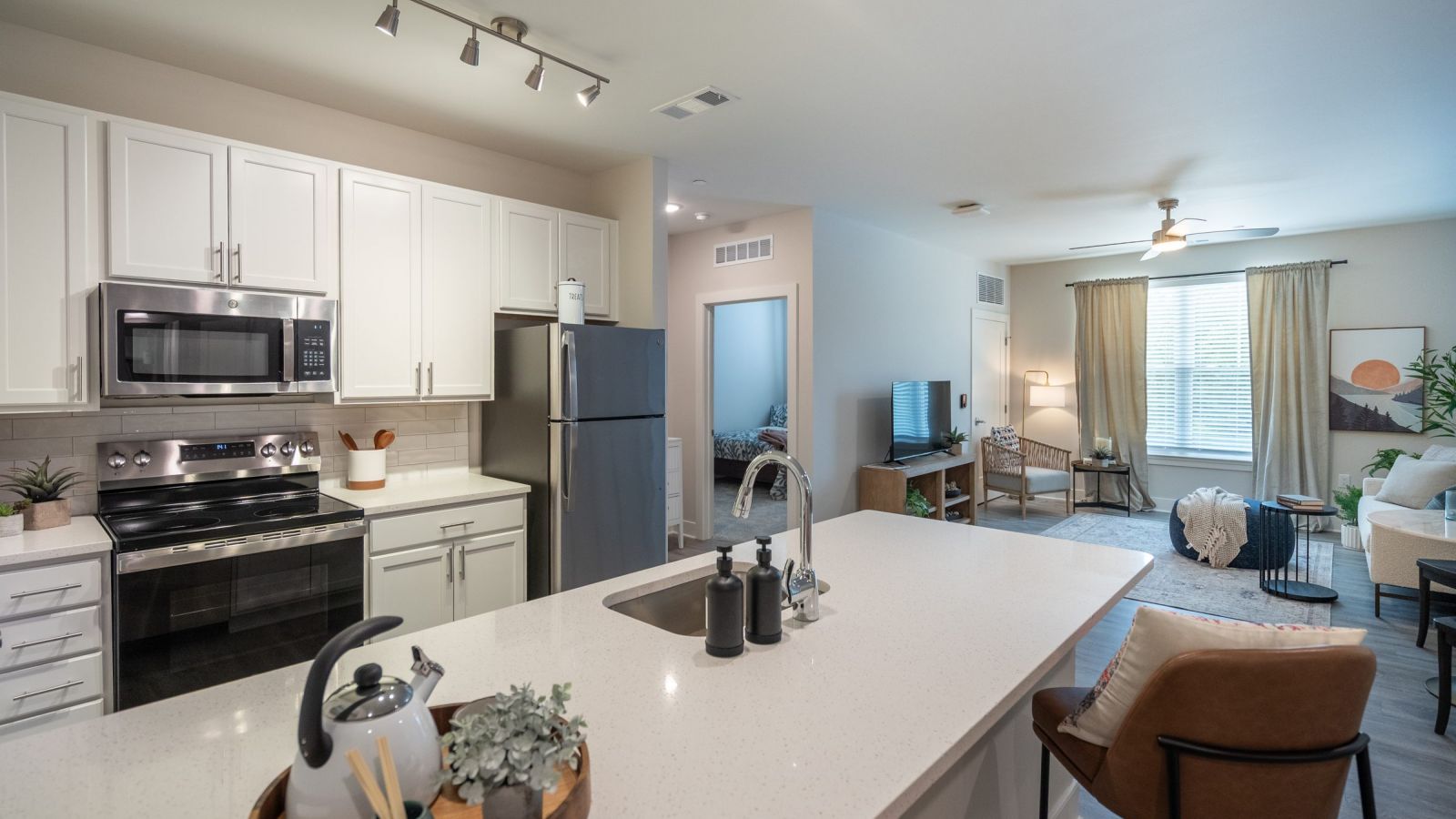 Modern kitchen and living area with white cabinets, stainless steel appliances, and a large island. Cozy seating area with a sofa and rug in the background. Bright and inviting atmosphere.