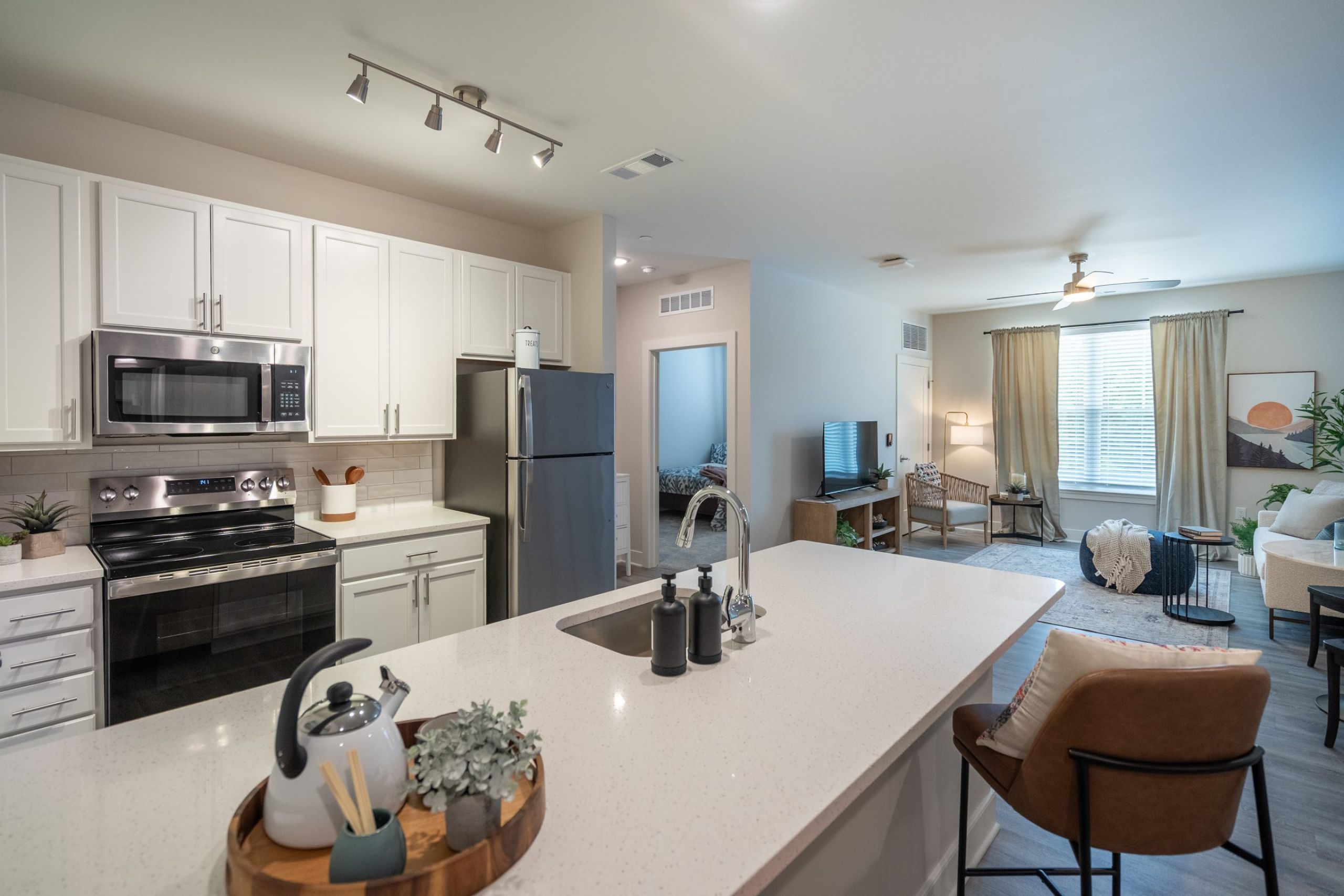 Acclaim at Greenbrier apartment homes with Modern kitchen with white cabinets and an open view into a bright living room with large windows and decor.