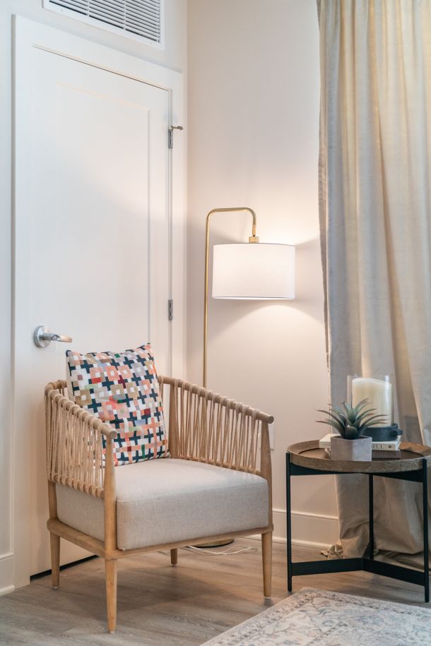 Acclaim at Greenbrier apartment homes with A cozy armchair with a patterned pillow sits beside a round table and floor lamp in a softly lit room.
