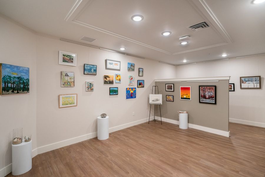 Acclaim at Greenbrier apartment homes with Art gallery room with various colorful paintings and drawings displayed on neutral walls with wood flooring.
