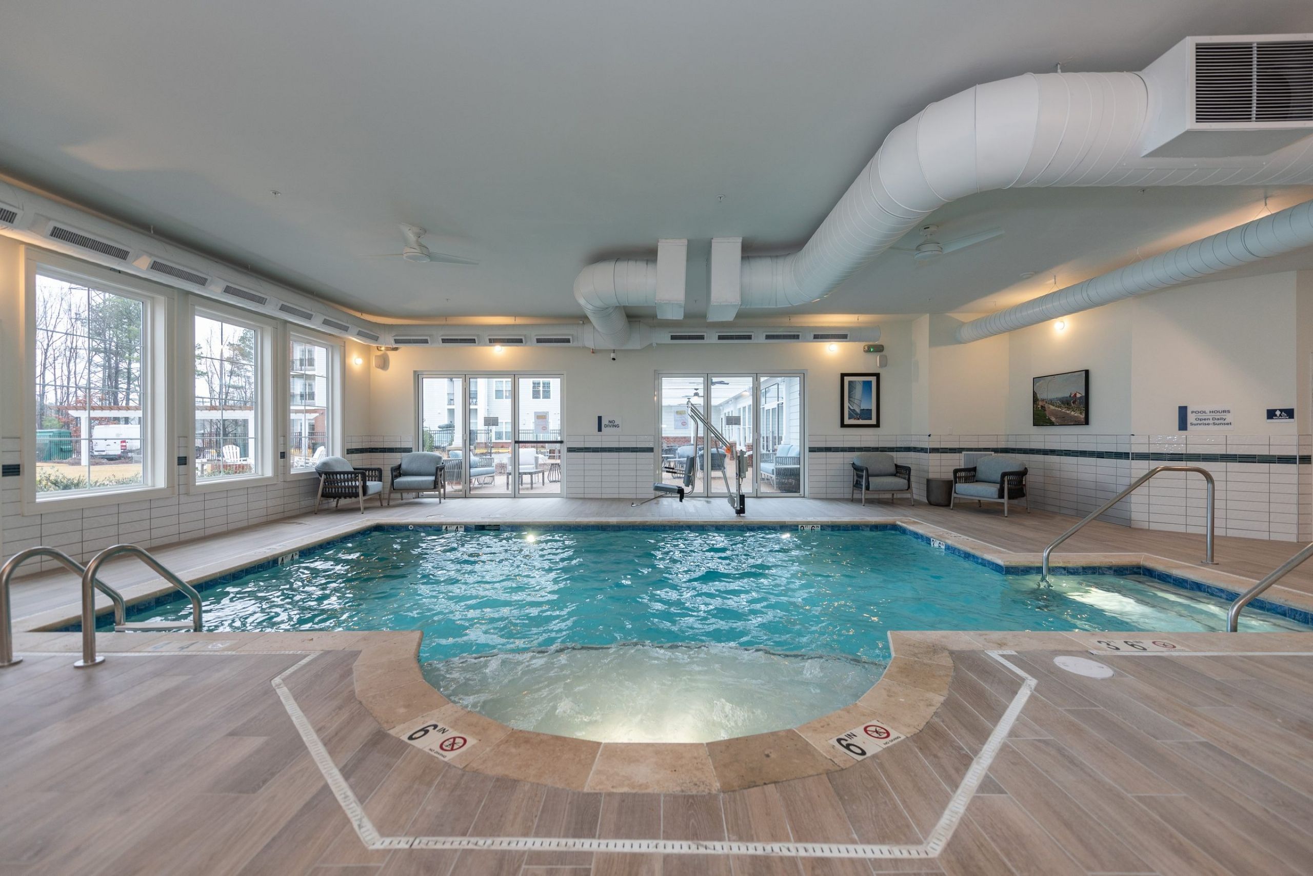 Acclaim at Greenbrier apartment homes with Indoor swimming pool with large windows, lounge chairs, and wooden floors in a bright, modern room.