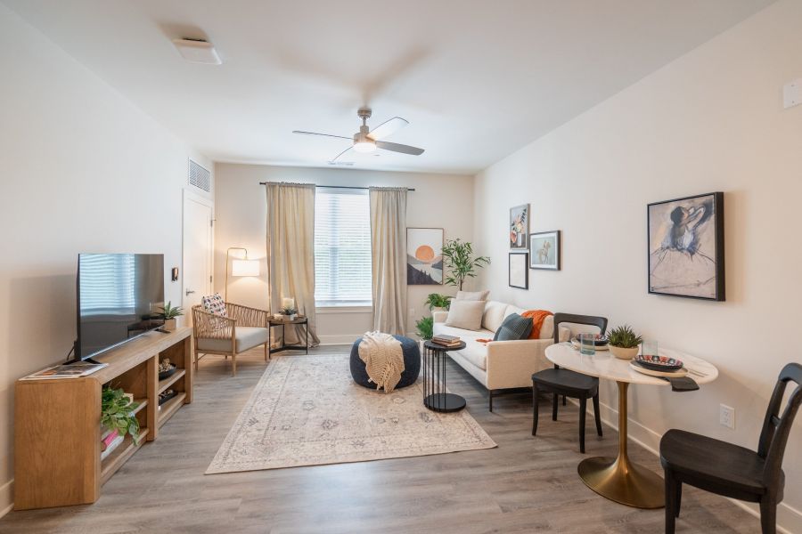 Acclaim at Greenbrier  apartment homes with Modern living room with a sofa, TV, round table, artwork, and large window with beige curtains.