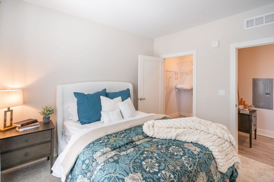 Acclaim at Greenbrier apartment homes with Bright bedroom with a neatly made bed, open closet door, nightstand, and cozy blanket on the bed.
