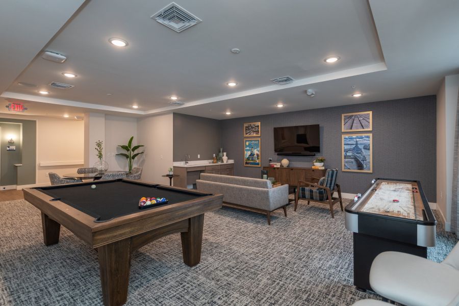 Acclaim at Greenbrier apartment homes with Modern game room with a pool table, shuffleboard, sofas, TV, and wall art on gray and blue walls.
