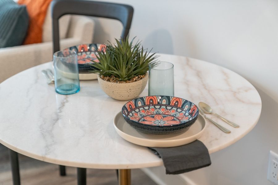 Acclaim at Greenbrier apartment homes with A round marble table set for two with patterned plates, blue glasses, and a potted succulent centerpiece.