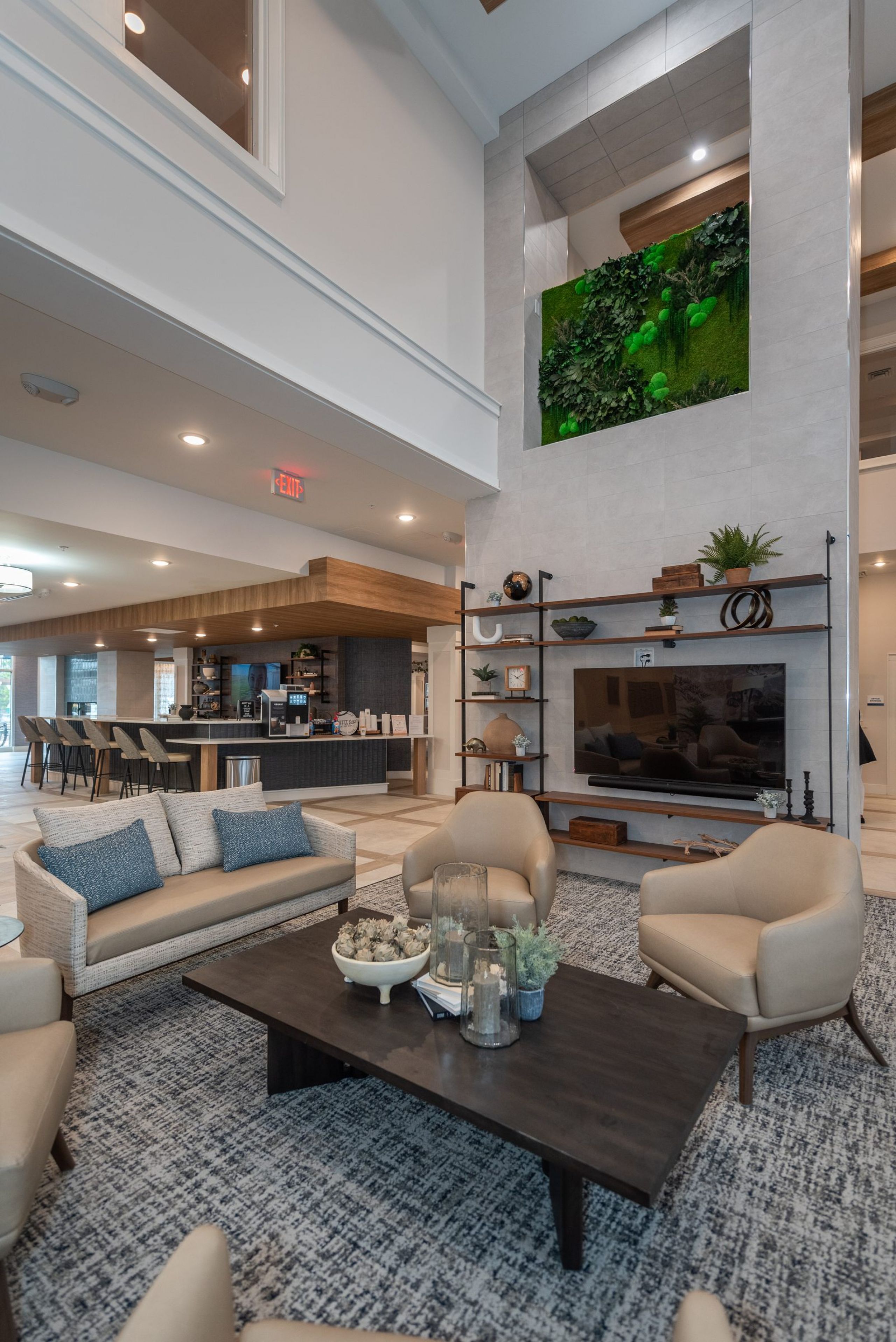 Acclaim at Greenbrier apartment homes with Modern lounge with beige chairs, a dark coffee table, TV, open shelving, and a green wall above the fireplace.