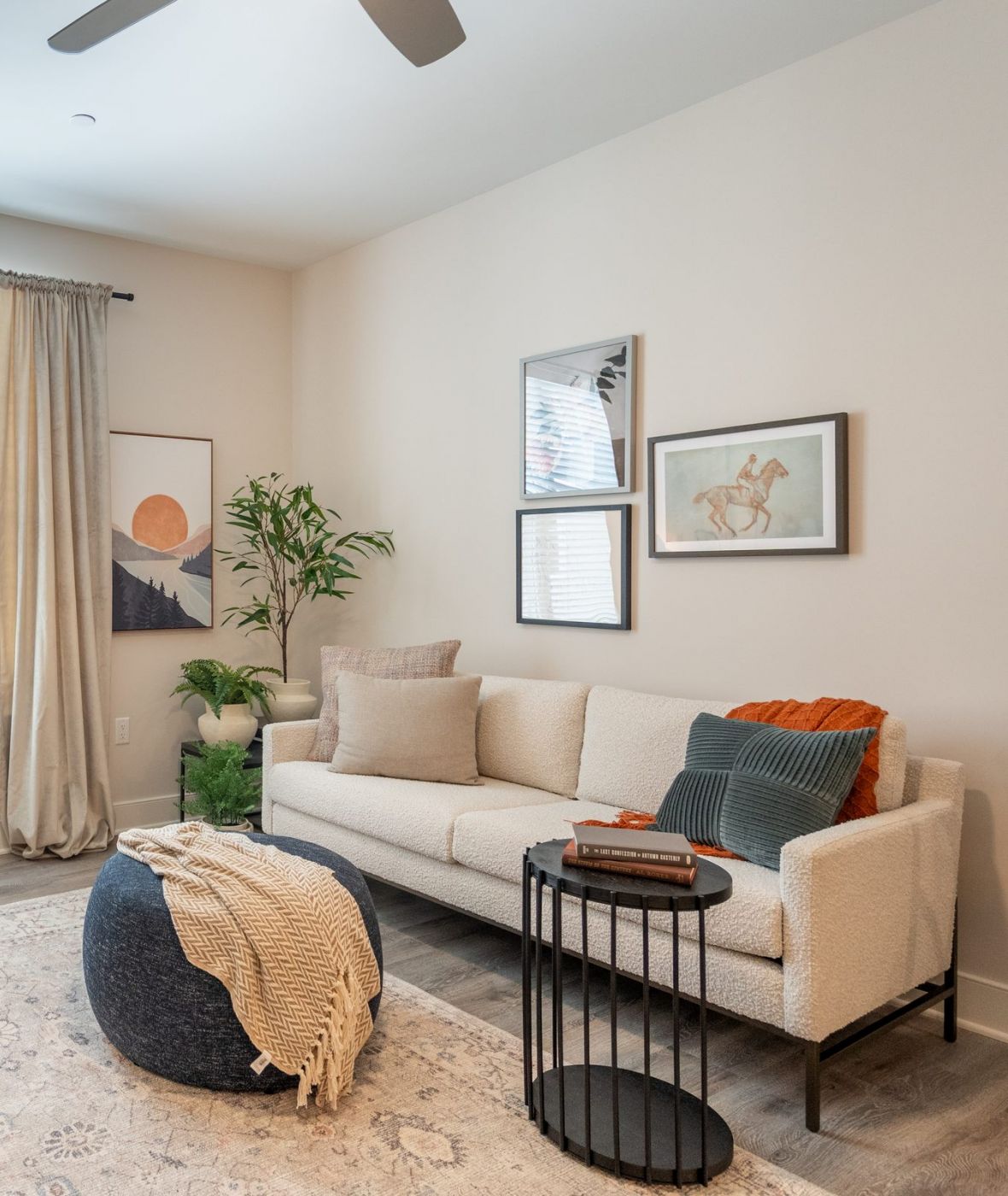 Acclaim at Greenbrier apartment homes with Cozy living room with a sofa, armchair, pouf, side table, window with curtains, and wall art.