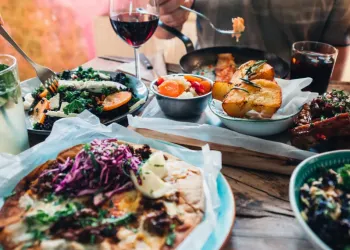 A table filled with assorted dishes, salads, drinks, and a person eating with a fork.