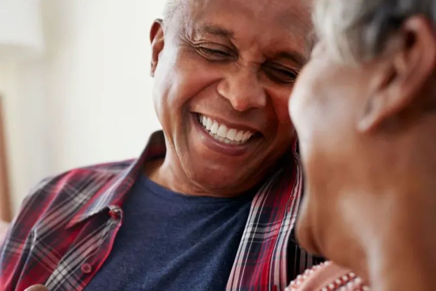 Older man and woman smiling and laughing together, man holding a white mug.
