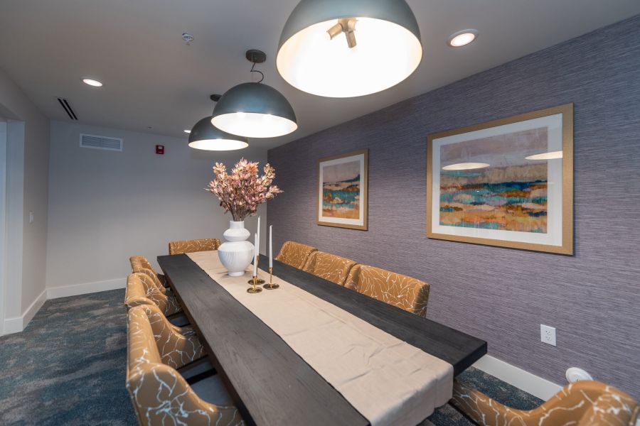 Acclaim at Greenbrier apartment homes with Modern dining room with a long table, patterned chairs, and wall art under large pendant lights.