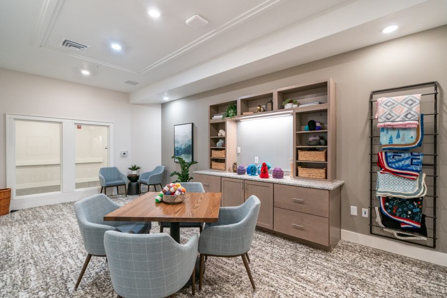 Acclaim at Greenbrier apartment homes with Craft room with a table, four chairs, shelves with baskets and yarn, and a rack displaying colorful blankets.