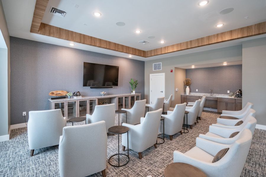 Acclaim on Greenbrier apartment homes with Modern meeting room with rows of white chairs facing a large TV on the wall, with side tables and decor.