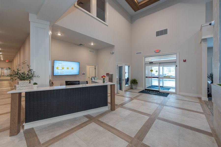 Acclaim at Greenbrier apartment homes with Modern hotel lobby with a reception desk, tiled floor, large windows, and automatic glass doors.