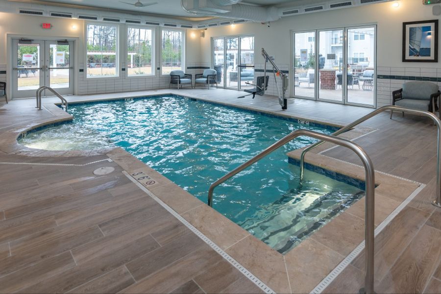 Acclaim at Greenbrier apartment homes with Bright indoor pool room with lounge chairs, large windows, and pool lifts for accessibility.