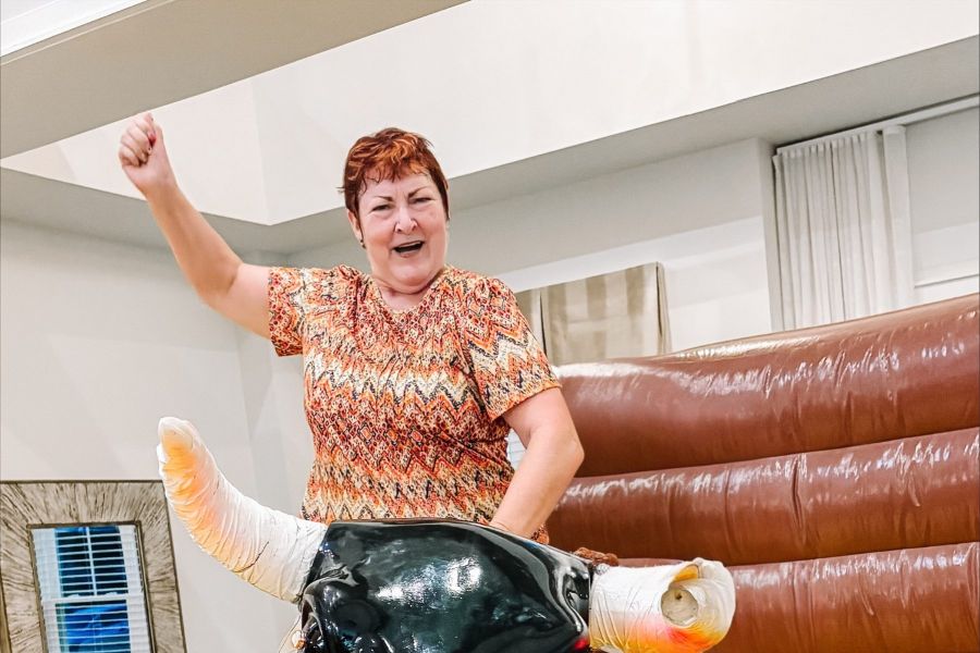 Attain at Greenbrier apartment homes with A smiling woman rides a mechanical bull indoors, raising one arm in excitement.