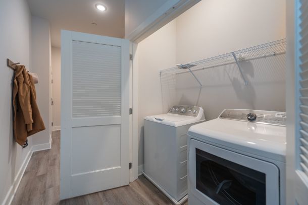 Acclaim at Greenbrier apartment homes with A laundry closet with a washer, dryer, open door, wire shelf, and a coat hanging on the wall.
