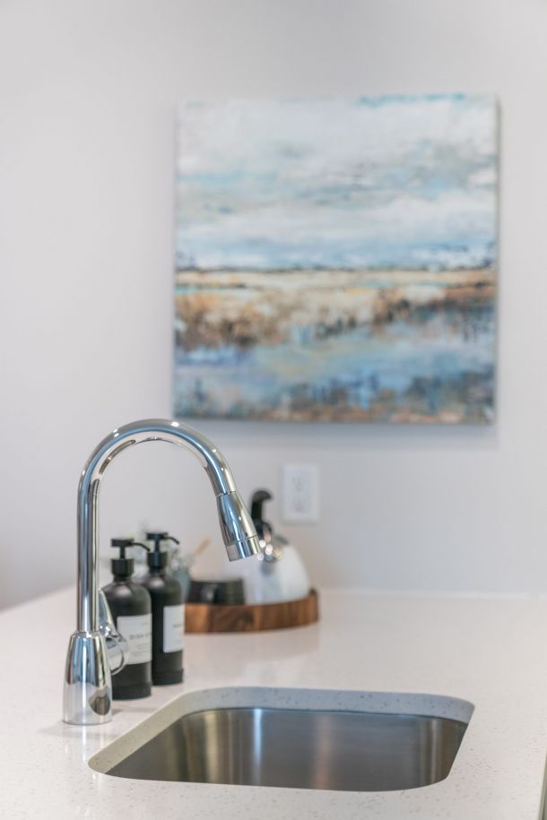 Acclaim at Greenbrier apartment homes with Modern kitchen sink with a chrome faucet, soap dispensers, and abstract art on the wall in the background.